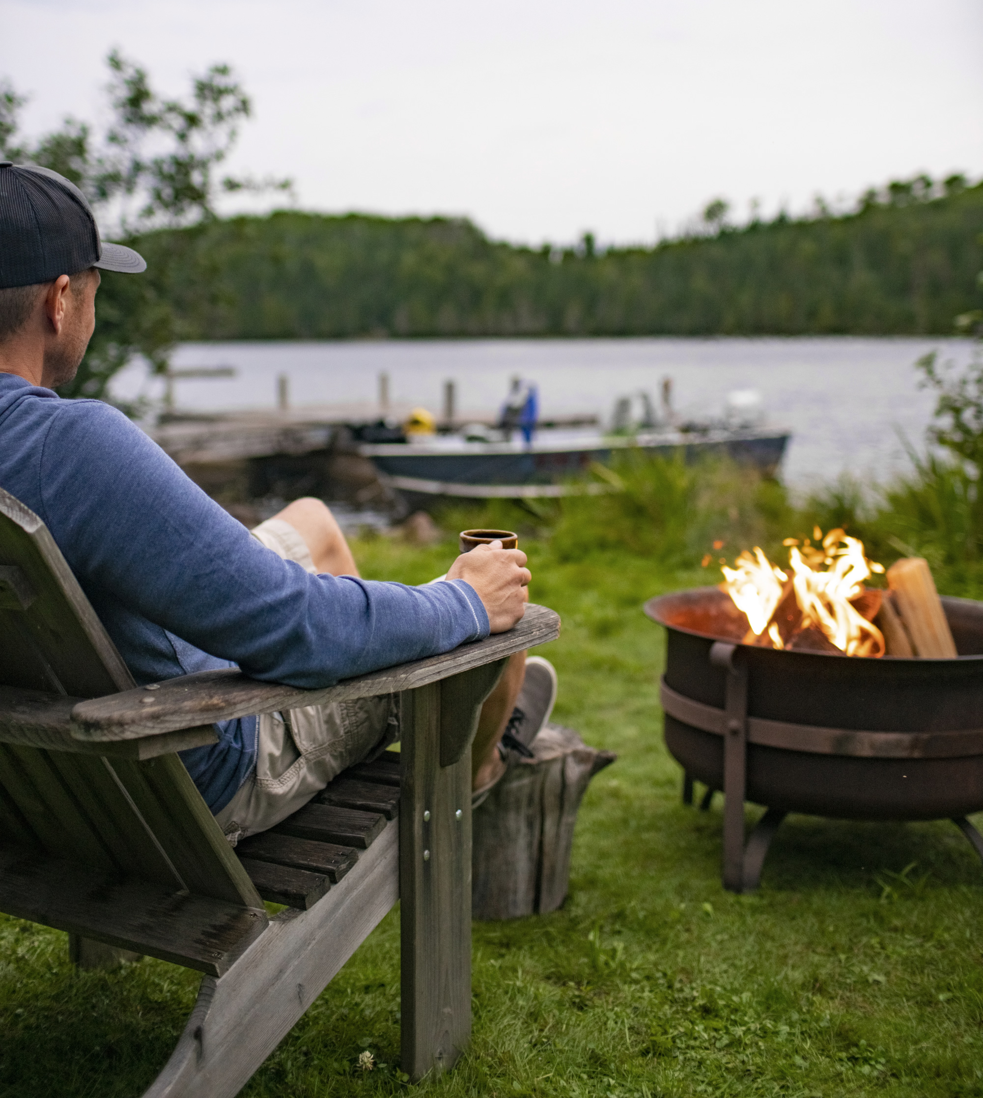 Man with coffee mug at campfire overlooking a lake