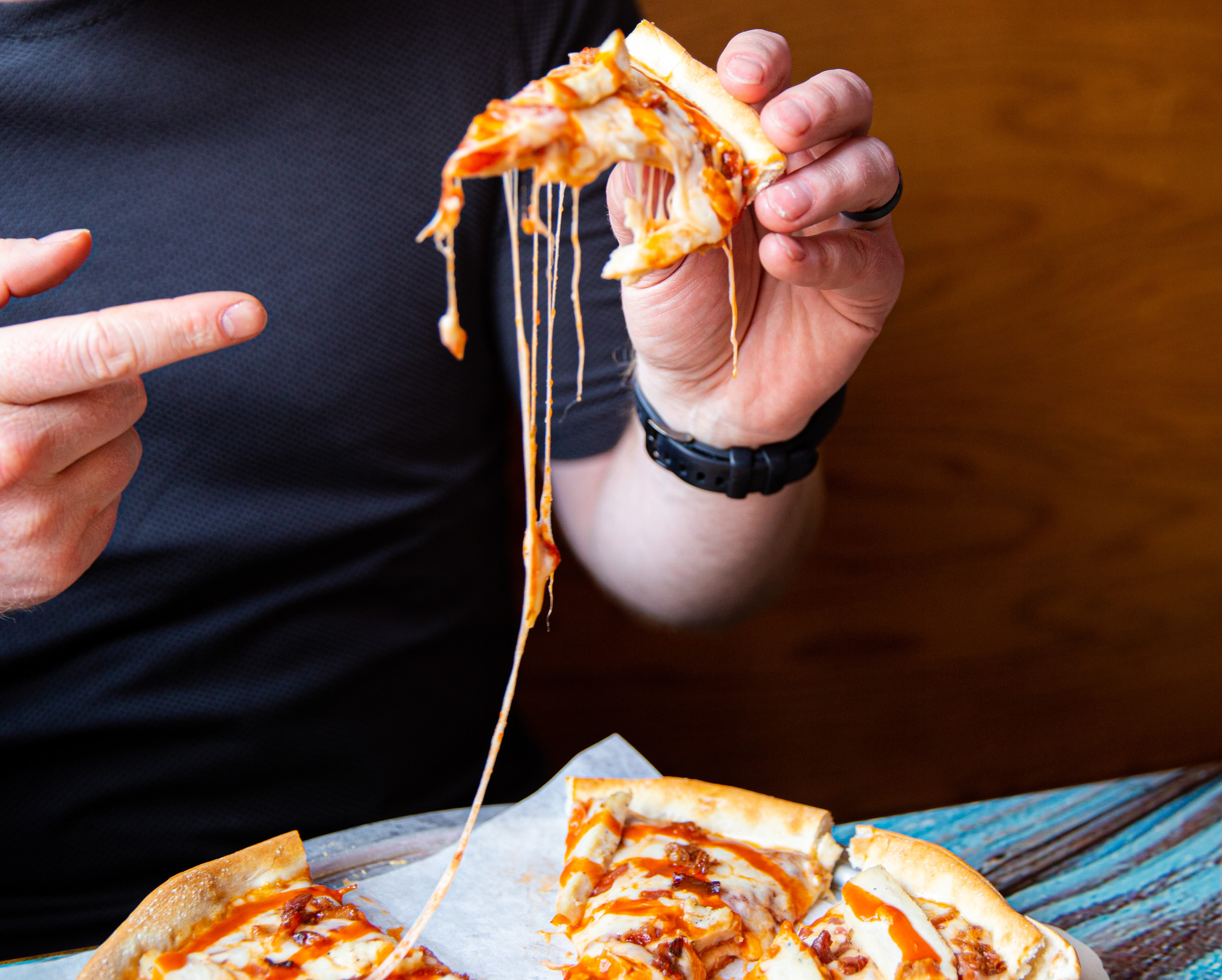 Man holding cheezy pizza slice at Zorbaz