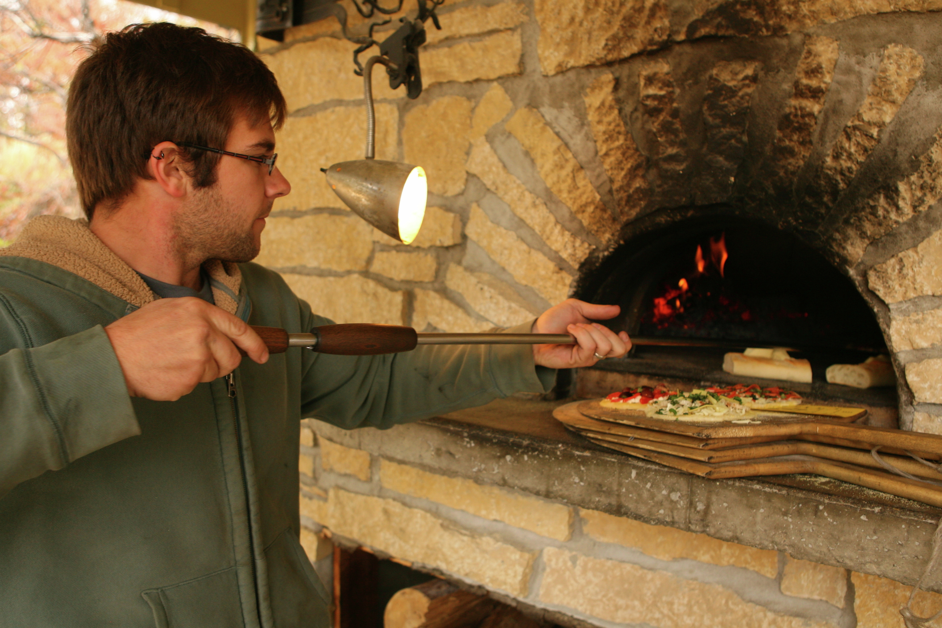 Man tending a wood-fired pizza oven
