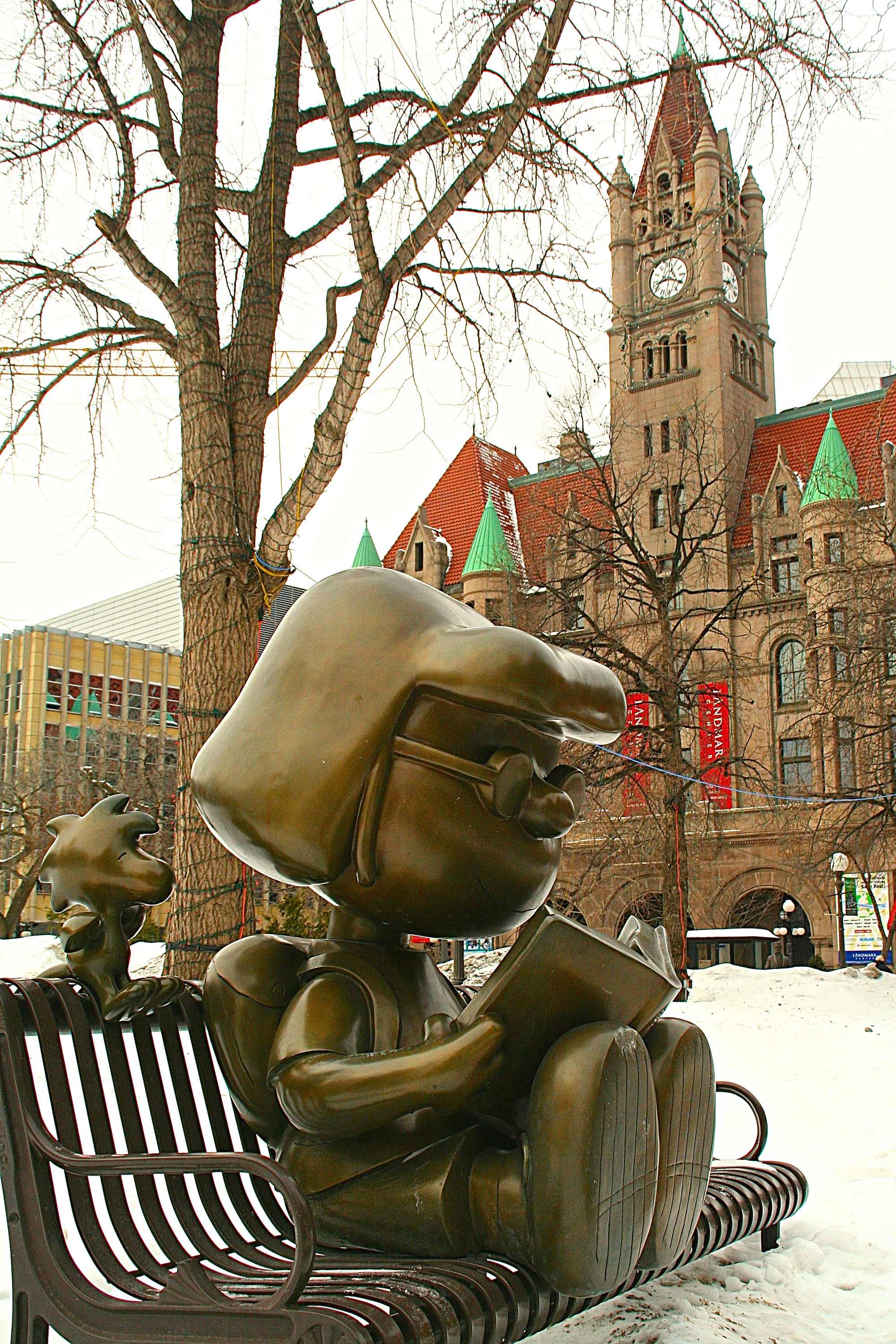 A bronze statue of a Peanuts character on a park bench in winter