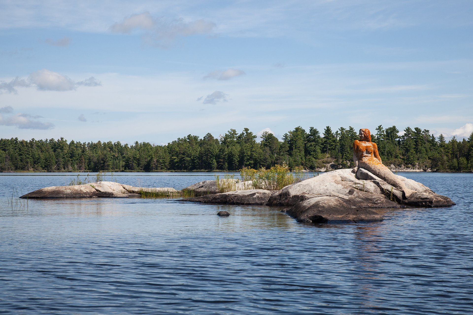A statue of a stone mermaid sits atop a rock formation in the middle of Rainy Lake in Voyeugers National Park