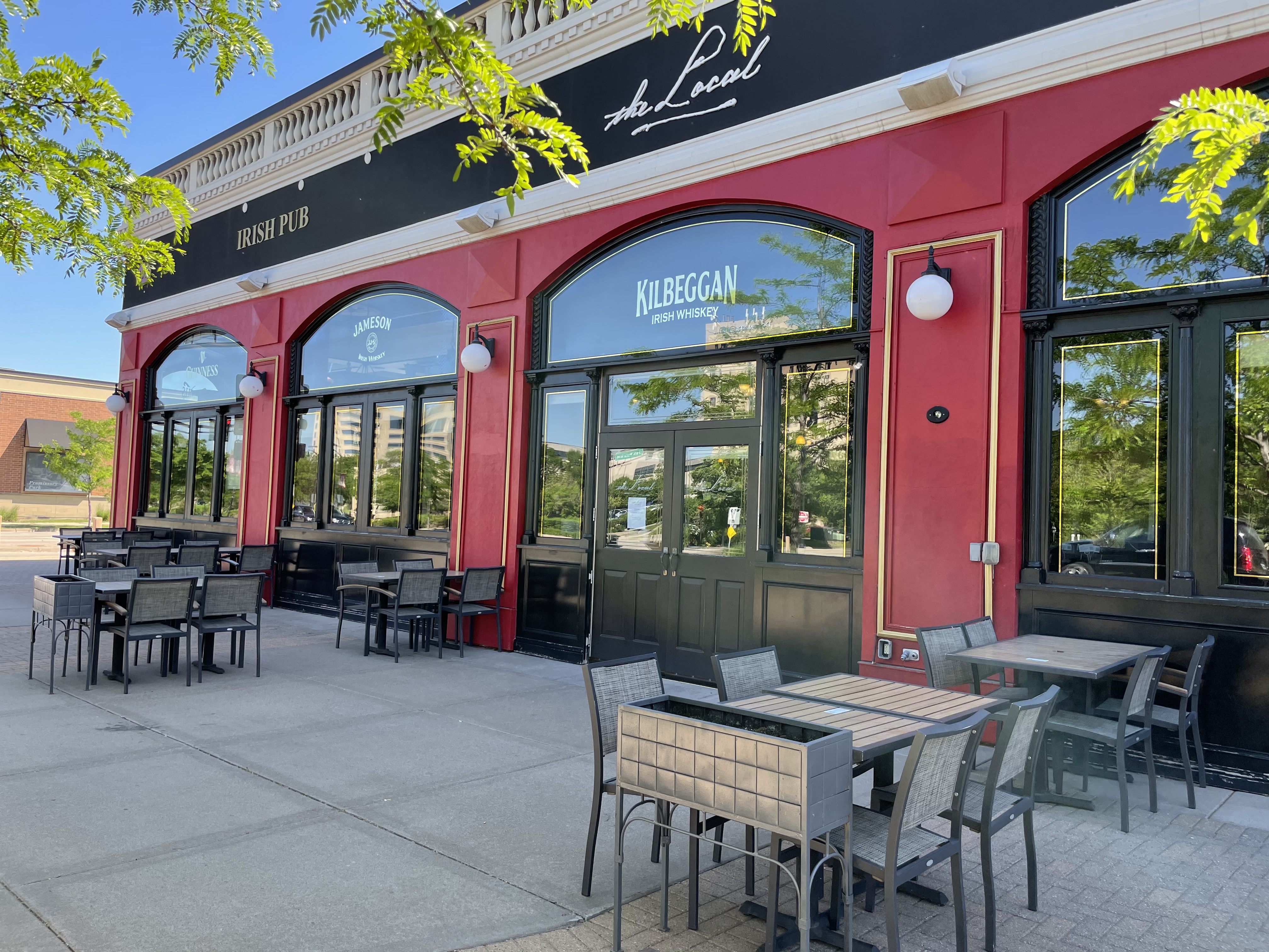 Exterior view of The Local, showing tables and shares on the sidewalk in summer