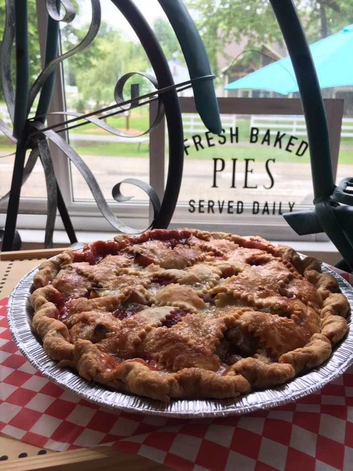 Fresh strawberry rhubarb pie with a pretty crosshatched crust sitting in fron window of Aroma Pie Shop