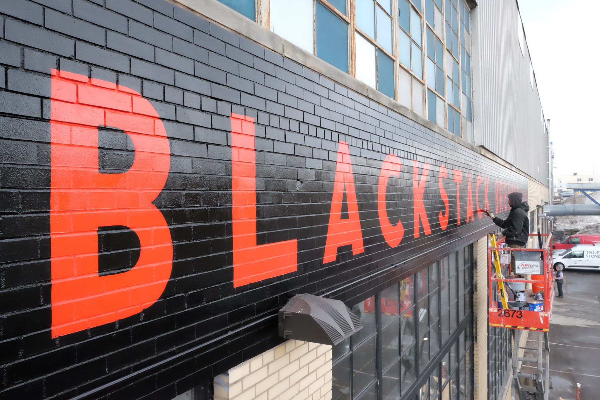 Dusty Signs paints the brick awning outside BlackStack Brewing