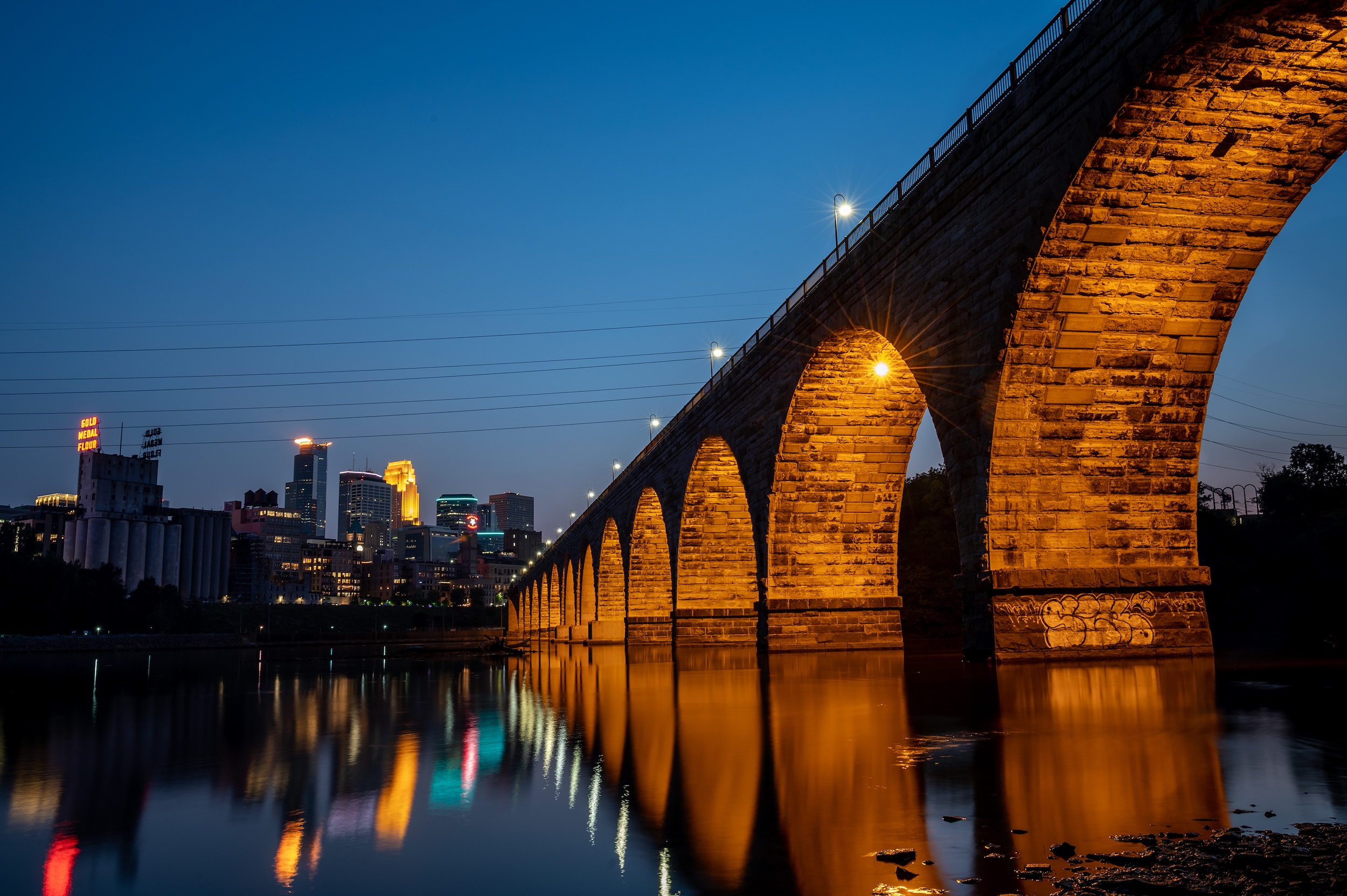 A nighttime landscape shot of Saint Anthony Main and the Stone Arch Bridge