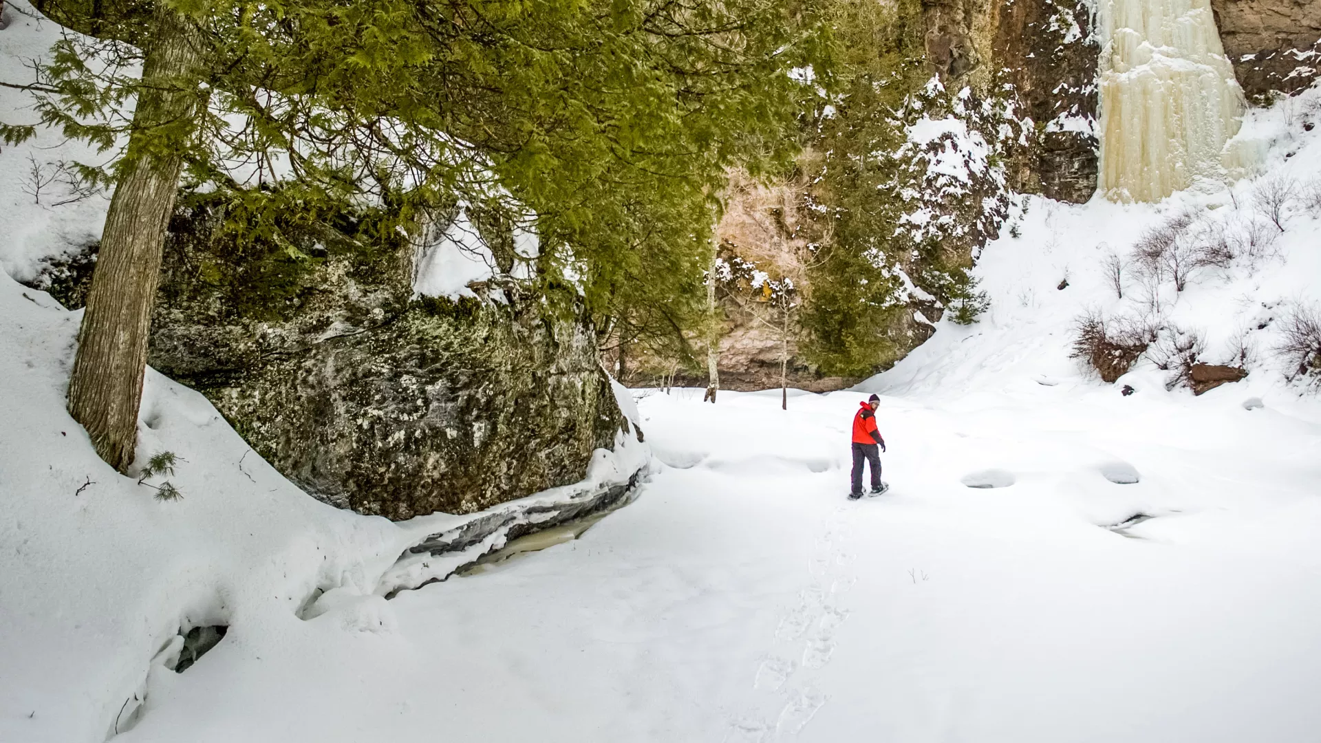 Man snowshoeing next to a frozen waterfall