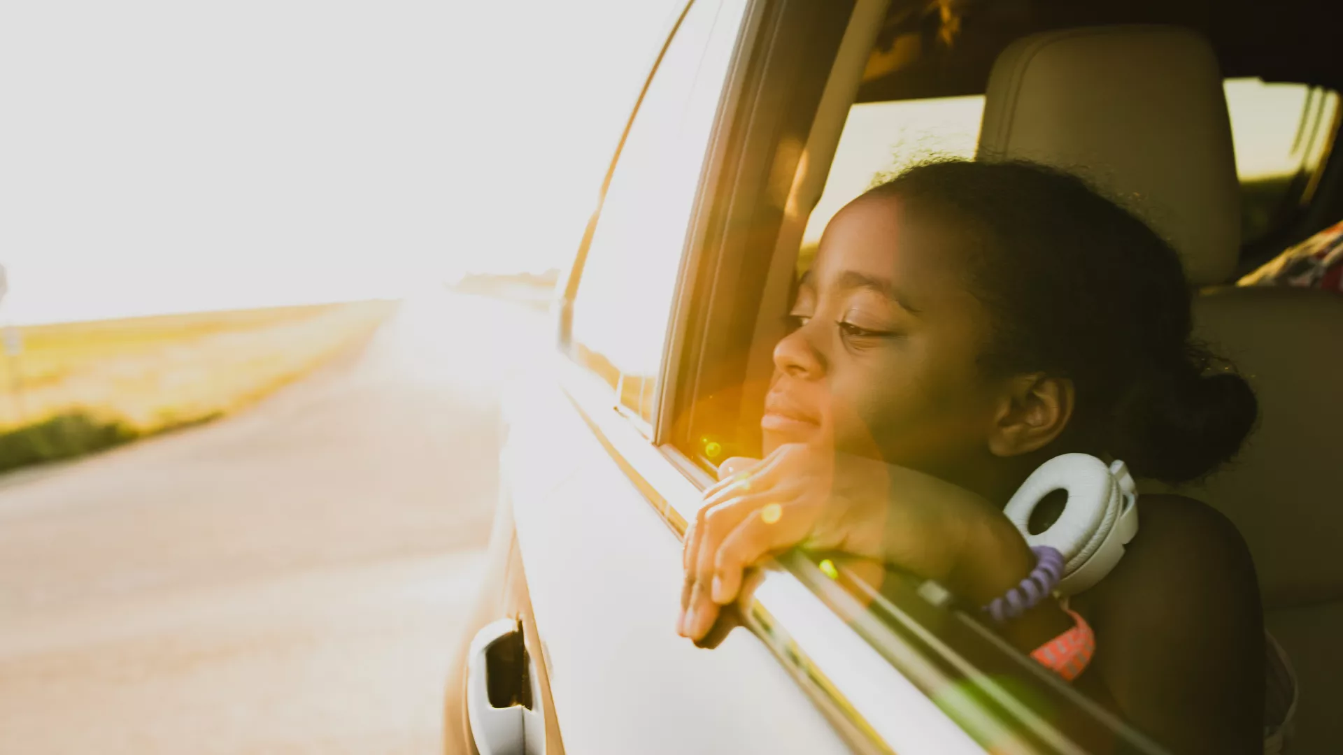 Girl looking out an open car window onto the open road