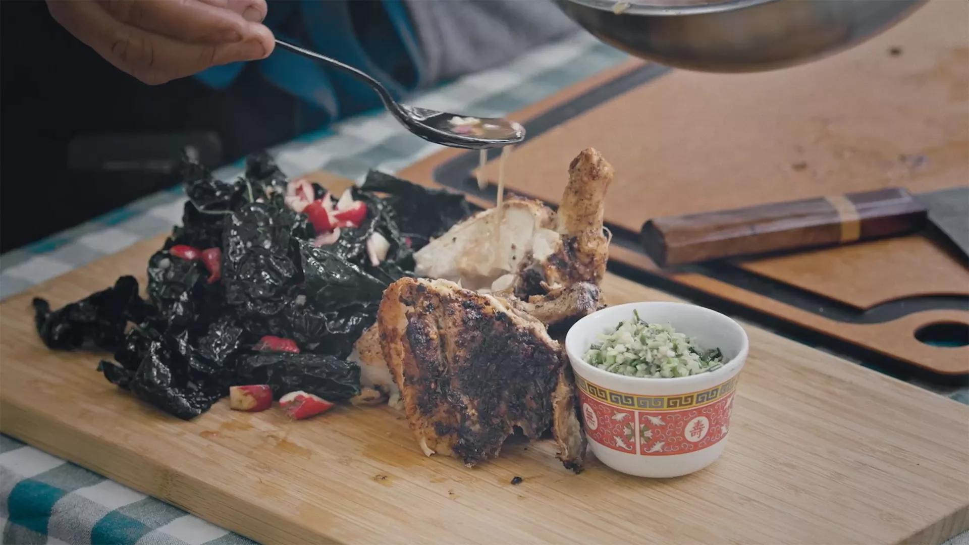 A mound of dark green kale salad, a grilled chicken leg, and a bowl of finely chopped sauce ingredients site side by side, ready to plate