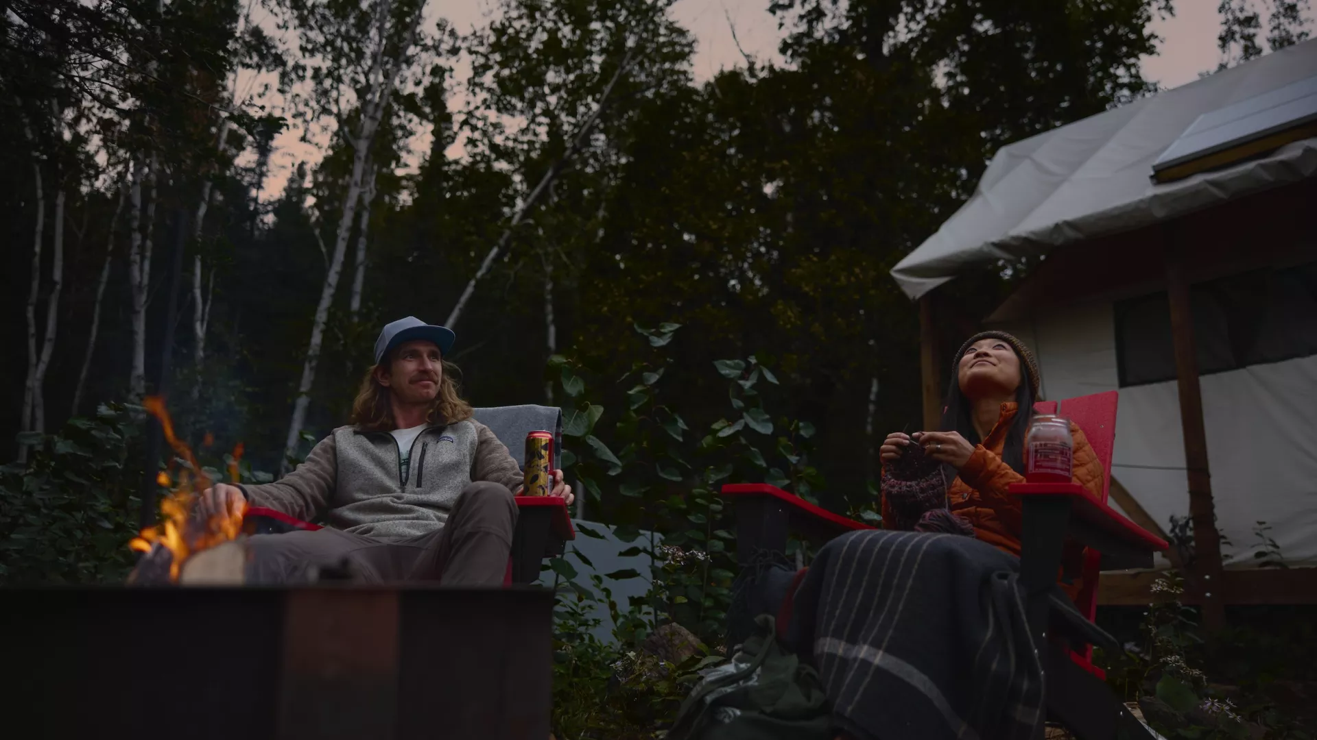 A couple sits beside a campfire at North Shore Camping Co in Beaver Bay