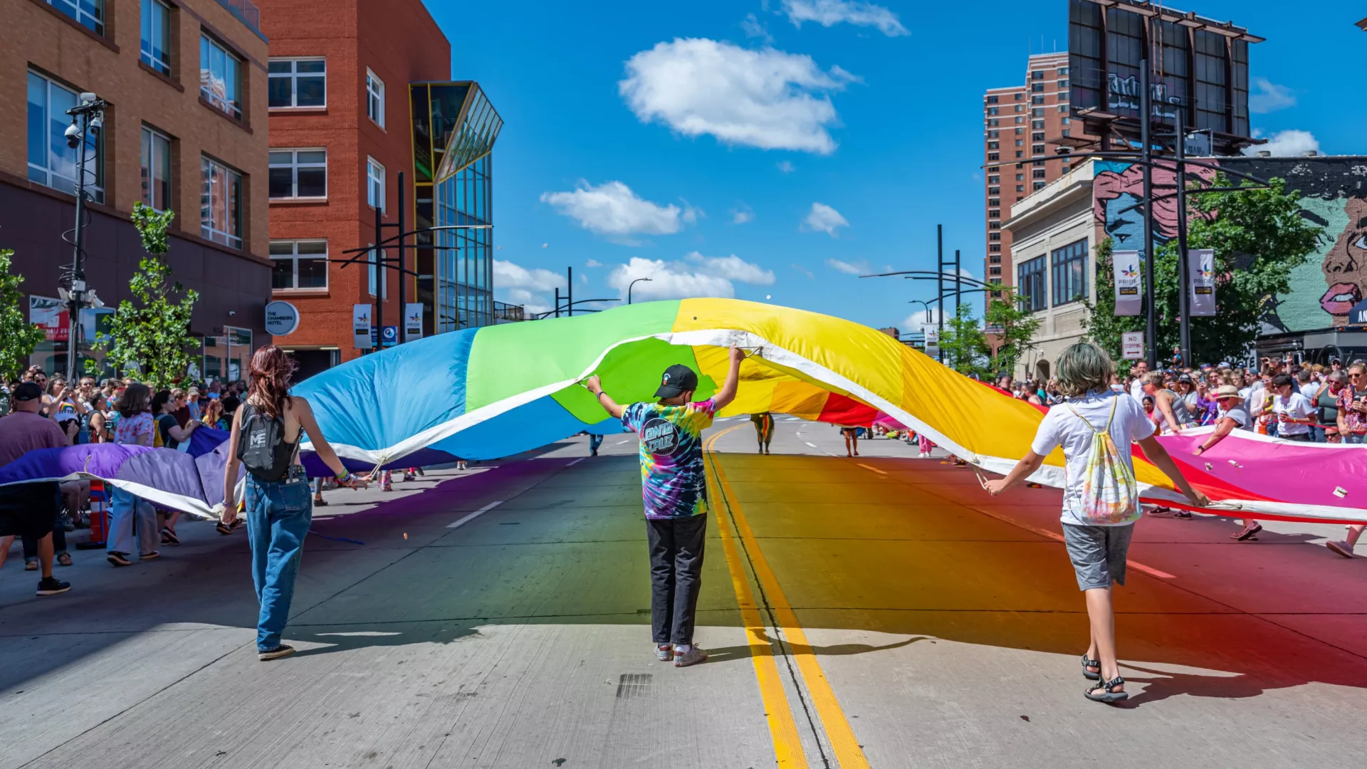 Three people unfurl a large rainbow flag at the Twin Cities Pride festival