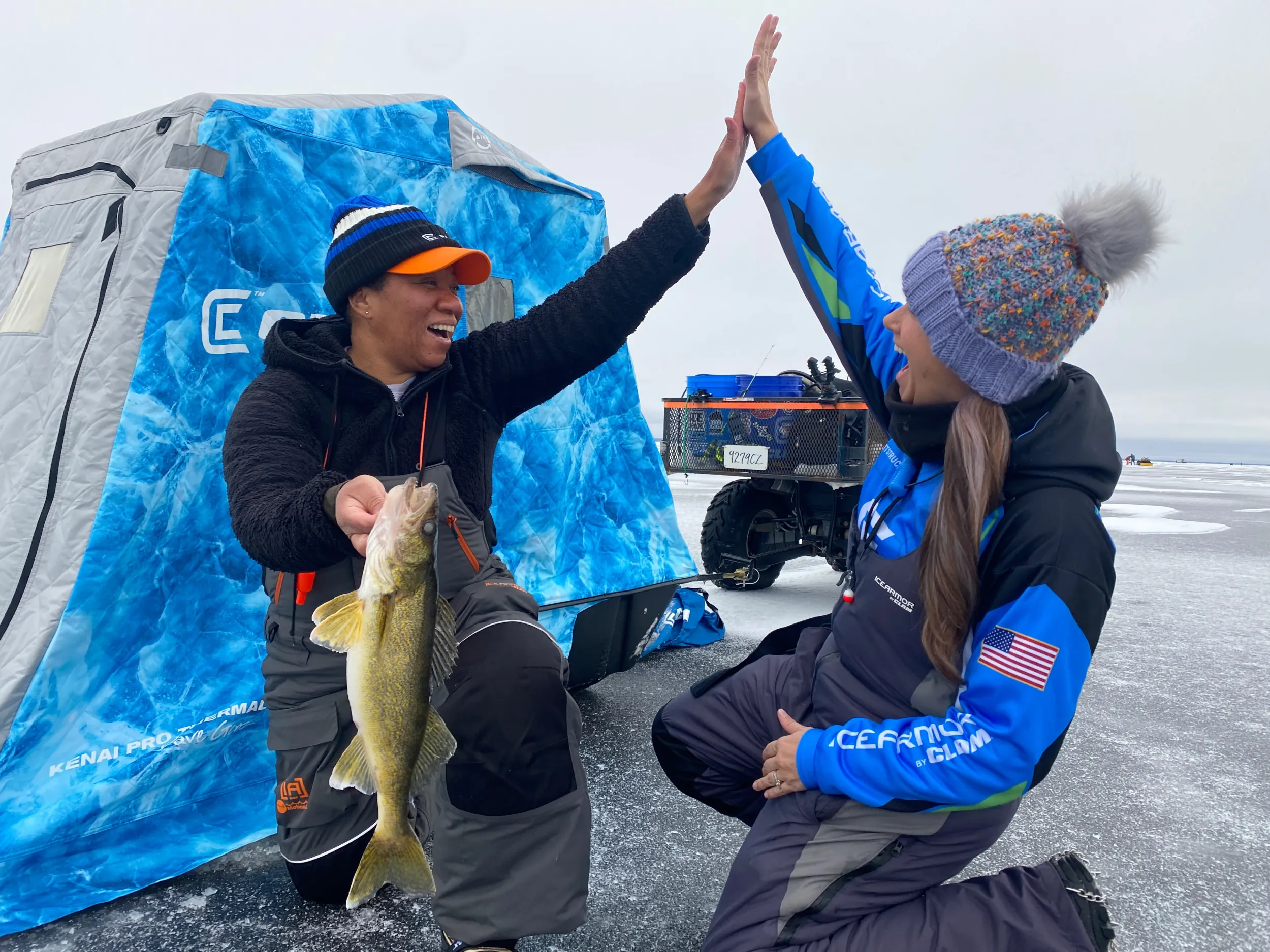 Two anglers high-five and show off a walleye they caught while ice fishing