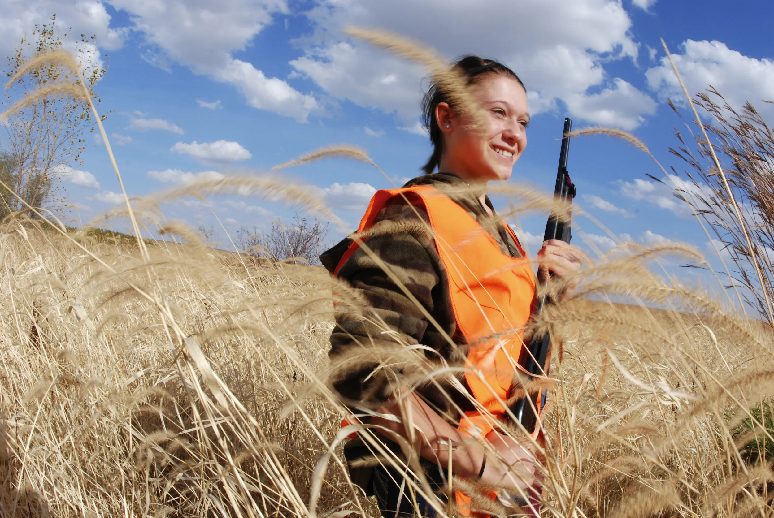 A woman stands in a field with a pheasant hunting rifle