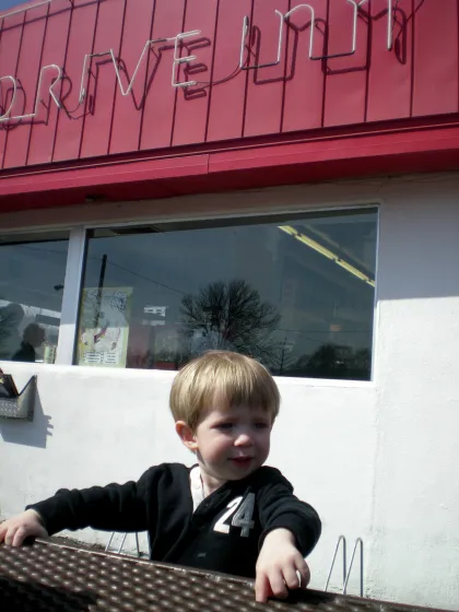 Un niño afuera de un restaurante tipo "drive in"