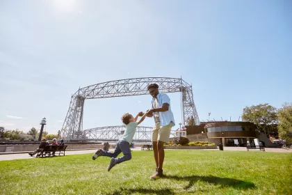 Father playfully spins his son around by the arms in front of the Duluth lift bridge