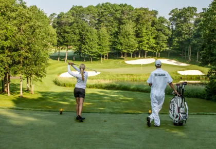 Woman golfing at The Classic at Madden's Resort while caddy holds her clubs