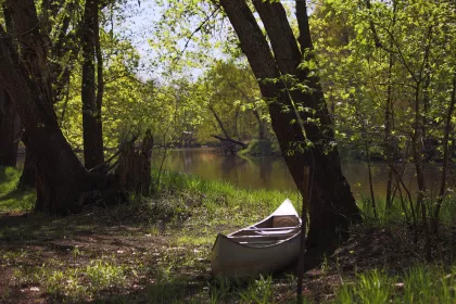 A canoe sits in the shadows onthe bank of the Rum River, Dappled sunlight through the trees as the river lazily drifts by in the background