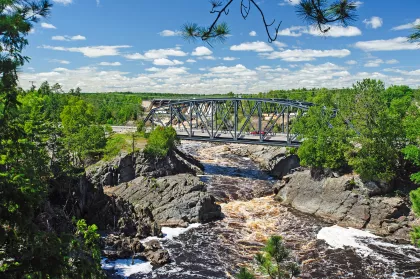 Car drives over a rushing river on a steel-latticed bridge