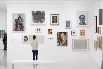 Man in front of gallery wall with numerous pieces of art at Walker Art Center