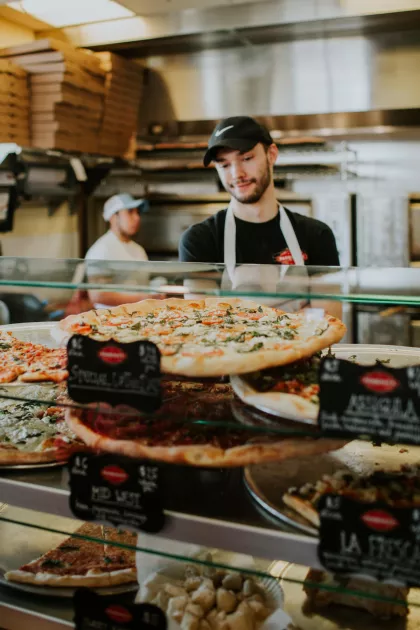 Pizzeria worker behind a deli case full of of pizzas