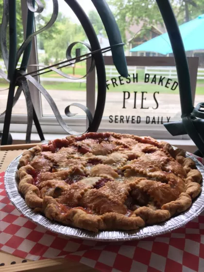 Fresh strawberry rhubarb pie with a pretty crosshatched crust sitting in fron window of Aroma Pie Shop