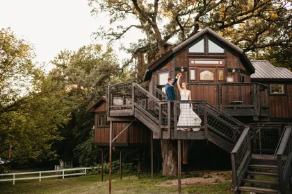 A married couple poses in front of the treehouse suite at Hope Glen Farm