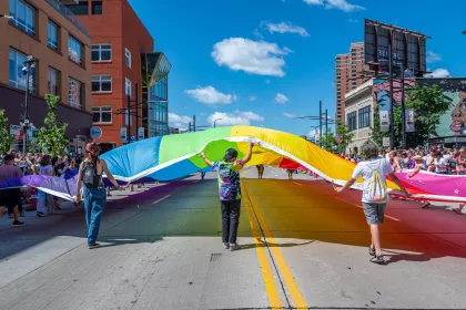 Three people unfurl a large rainbow flag at the Twin Cities Pride festival