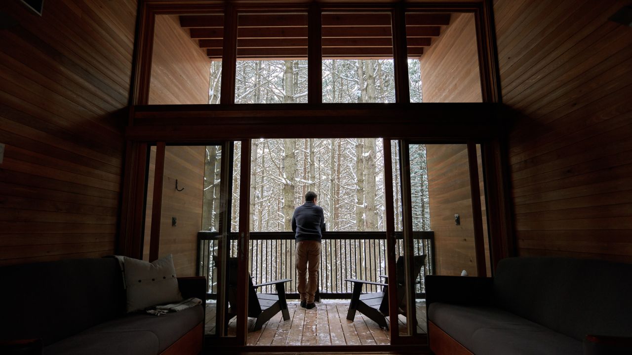 Hombre mirando hacia el bosque inviernal desde una cabaña