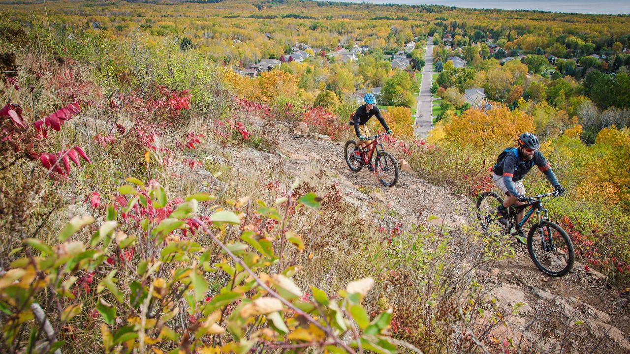 Two mountain bikers on a hill overlooking Duluth in fall