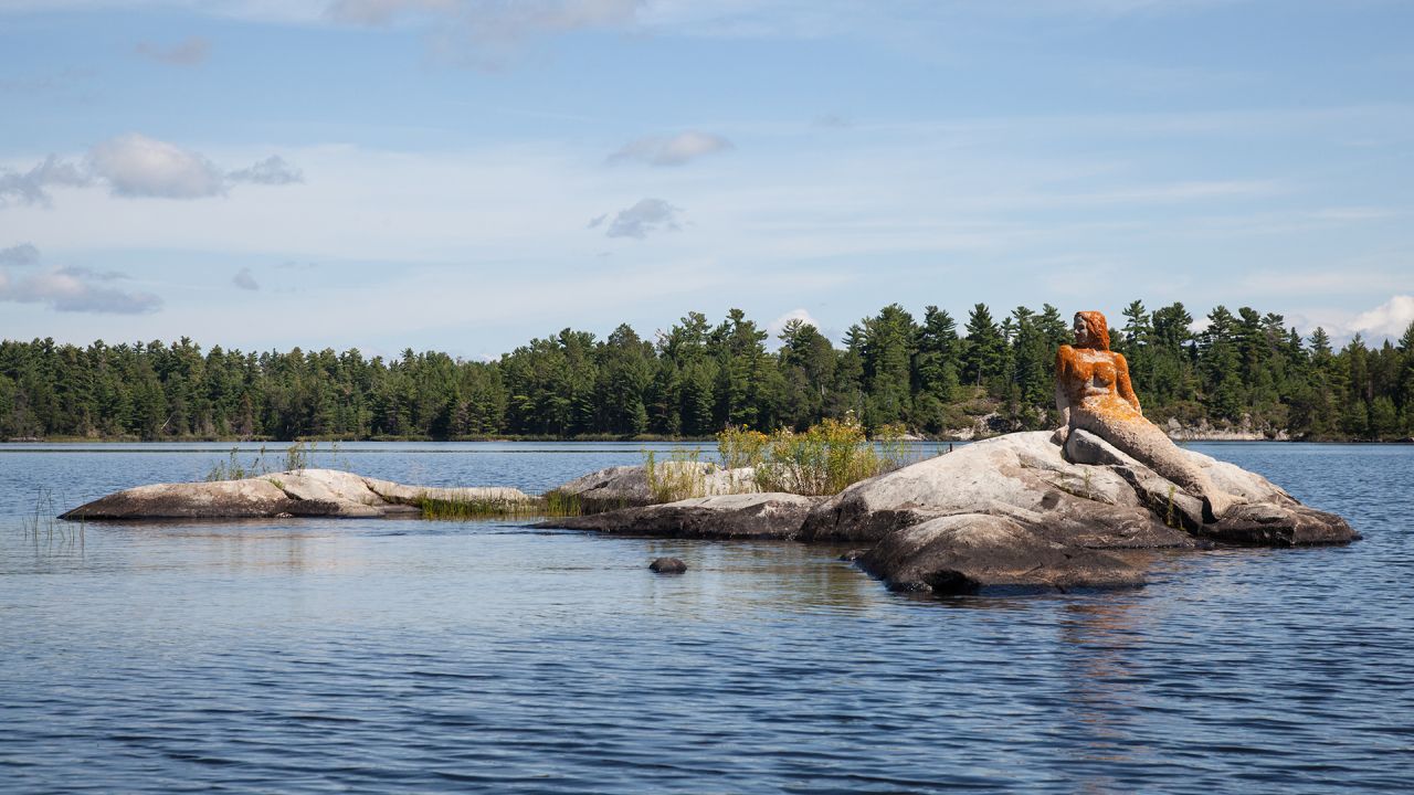 A statue of a stone mermaid sits atop a rock formation in the middle of Rainy Lake in Voyeugers National Park