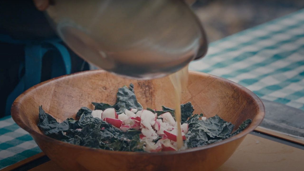 Chef Yia Vang pours homemade vinaigrette dressing on prepared kale salad as a side dish to his wood-fired Hilltribe Chicken dish