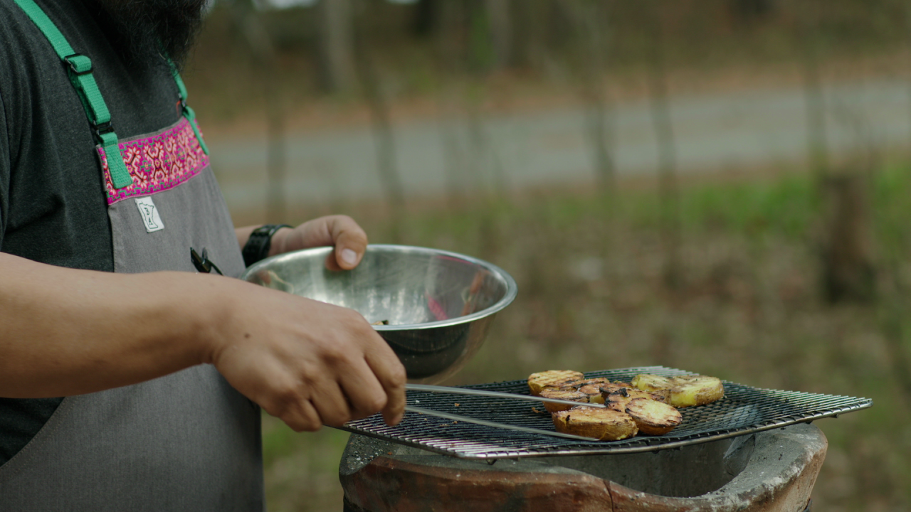 Yia Vang uses tongs to place par-cooked potato slices next to next to zucchini squash over a hot clay pot