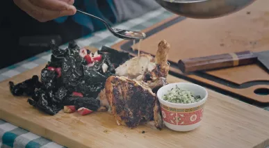 A mound of dark green kale salad, a grilled chicken leg, and a bowl of finely chopped sauce ingredients site side by side, ready to plate