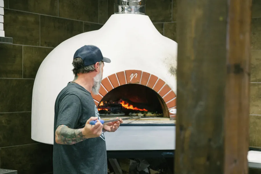 Man tends wood-fired pizza oven