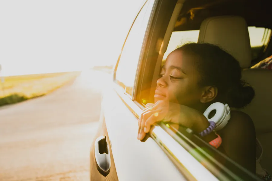 Girl looking out an open car window onto the open road