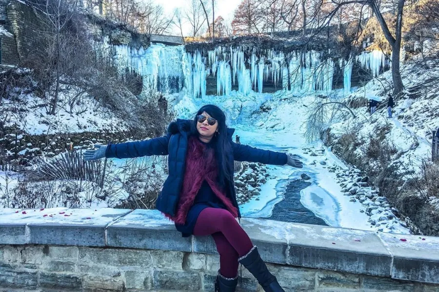 Woman sits on stone bridge in front of frozen waterfall