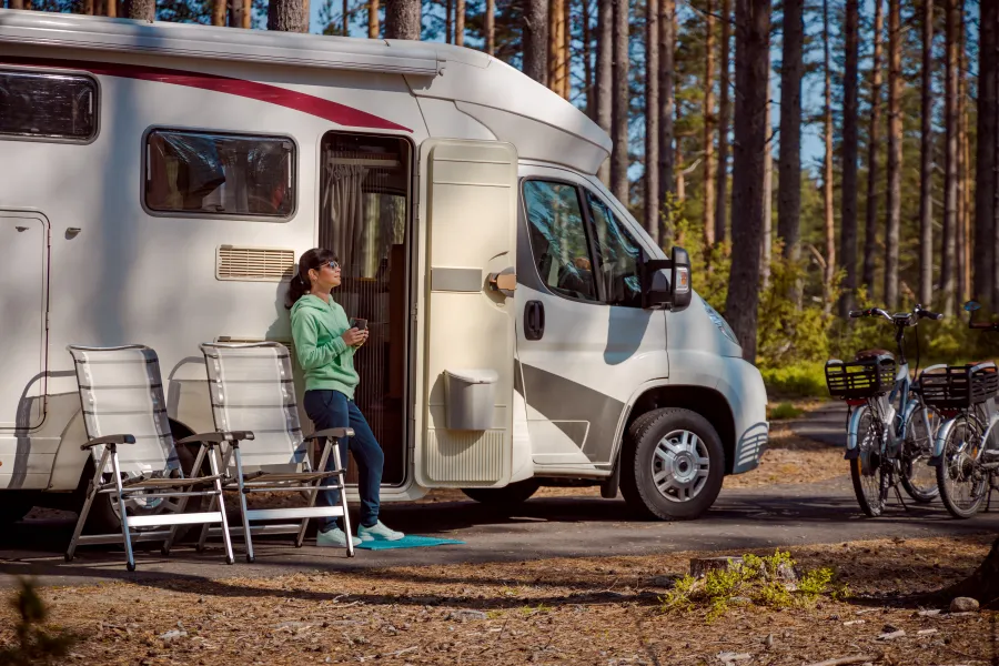 Woman stands by her RV with a cup of coffee, basking in the forest scenery