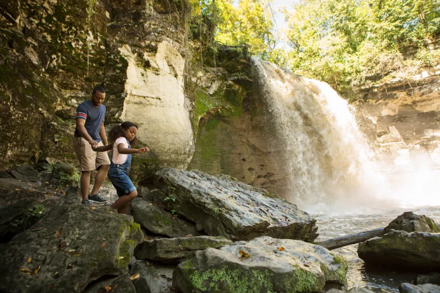 A father and daughter hike alongside Minneopa Falls
