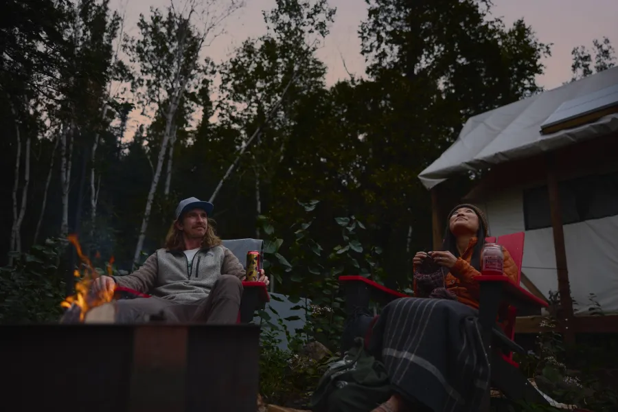 A couple sits beside a campfire at North Shore Camping Co in Beaver Bay