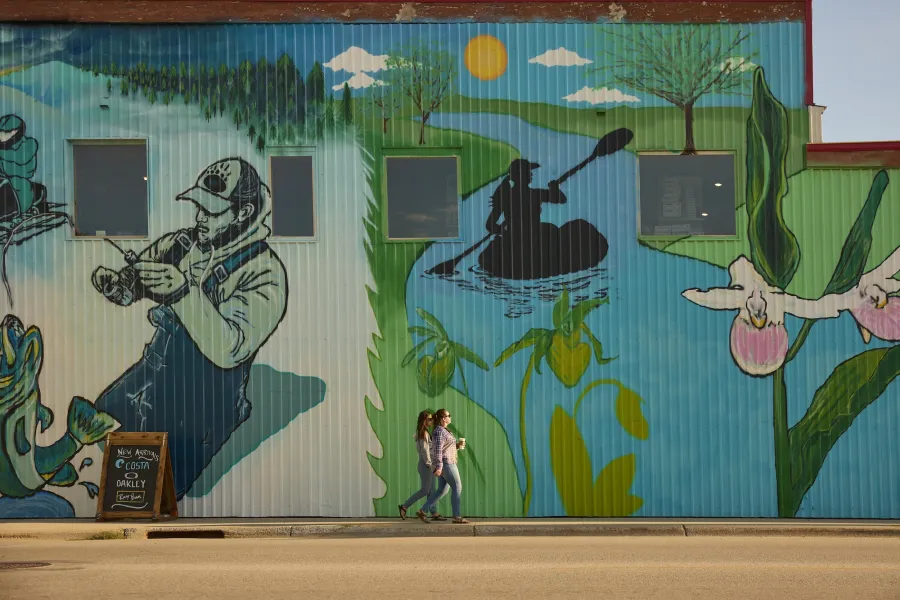 A couple friends walk in front of a Baudette mural