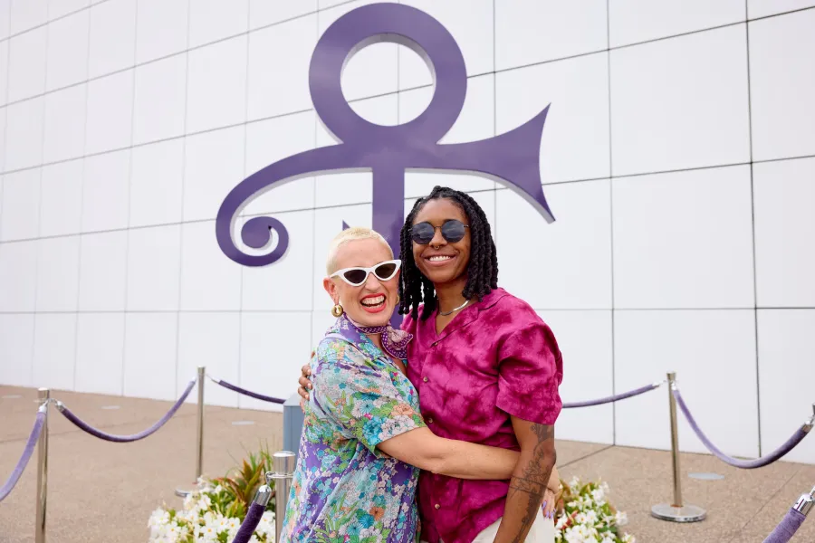 A couple stands in front of the Prince symbol at Paisley Park