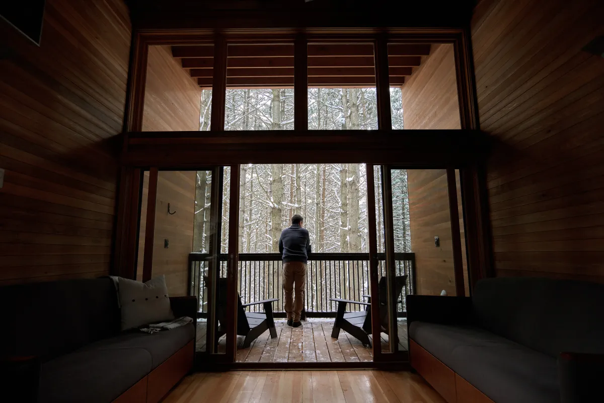 Man looking out into the winter woods from a camper cabin