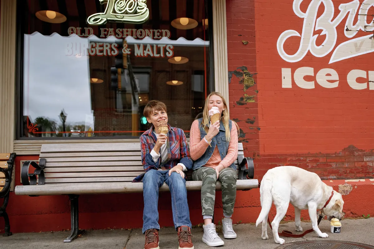 Two kids and dog eating ice cream on bench in Stillwater