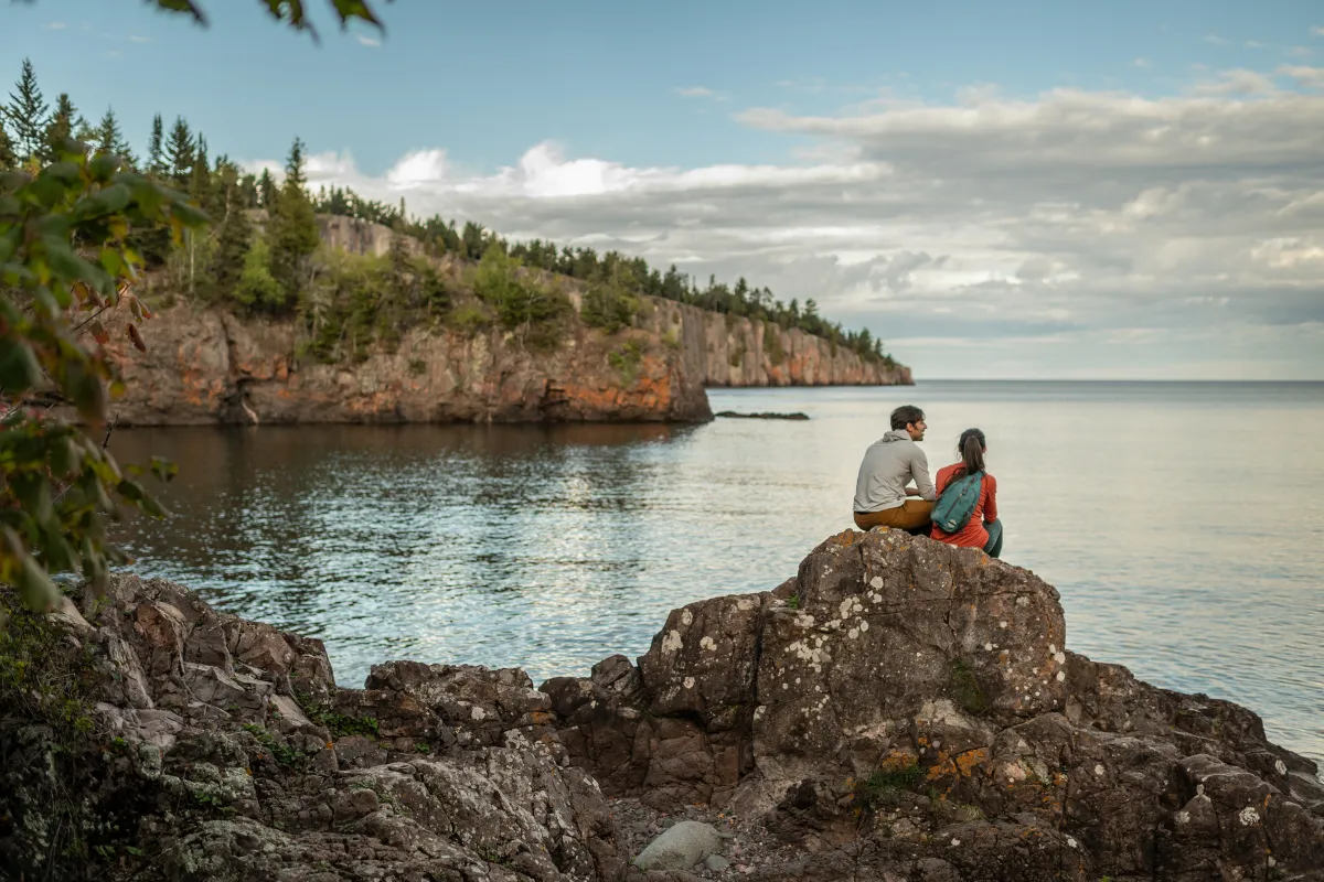 A pair of hikers sit on a rock overlooking Silver Bay in Tettegouche State Park