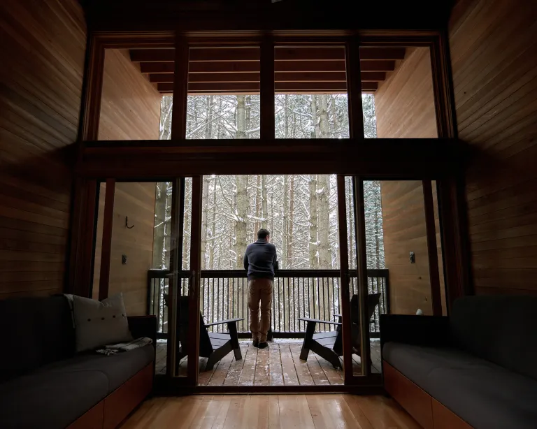 Man looking out into the winter woods from a camper cabin