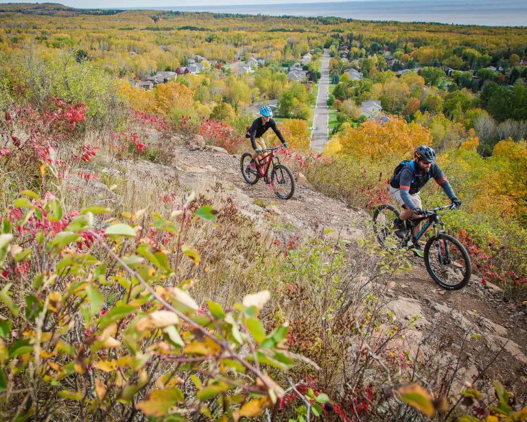 Two mountain bikers on a hill overlooking Duluth in fall