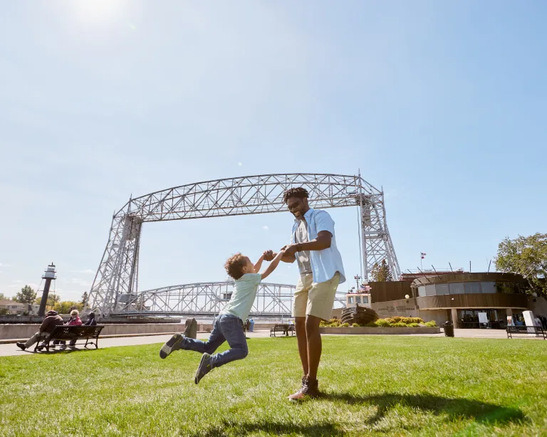 Father playfully spins his son around by the arms in front of the Duluth lift bridge