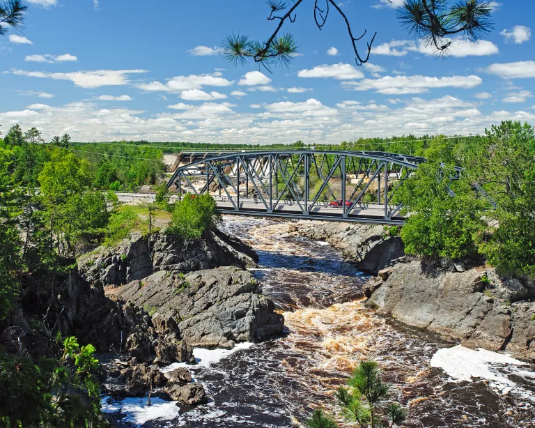 Car drives over a rushing river on a steel-latticed bridge