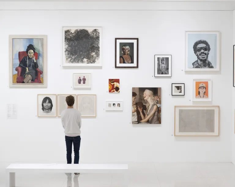 Man in front of gallery wall with numerous pieces of art at Walker Art Center