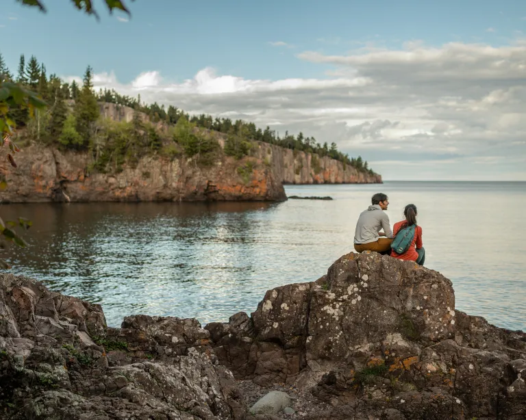 A pair of hikers sit on a rock overlooking Silver Bay in Tettegouche State Park